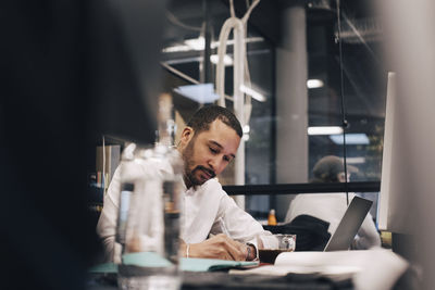 Businessman writing in diary at desk in office