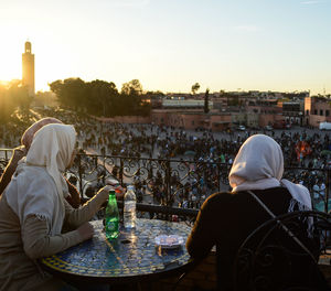 Rear view of couple sitting against buildings at sunset