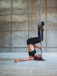 Full length of sensuous woman practicing pole dance in studio
