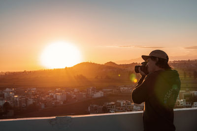 Man photographing cityscape against sky during sunset