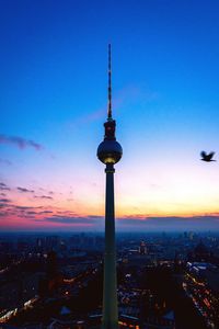 Communications tower in city against sky during sunset