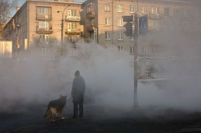 Rear view of person by dog on street with steam