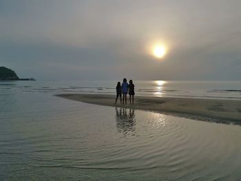 People at beach against sky during sunset