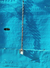 Padlock hanging from chain against blue metal