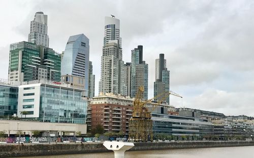 Modern buildings by river against sky in city