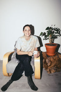 Portrait of smiling woman sitting on chair by plant at home