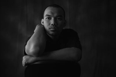 Portrait of young man sitting against wall