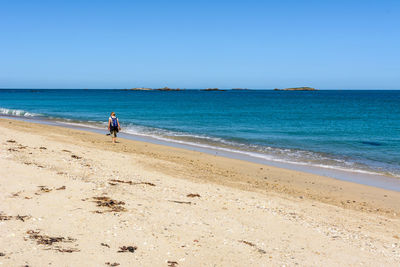 Scenic view of woman at beach against clear blue sky