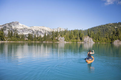 Attractive woman paddles stand up paddle board on blue lake.