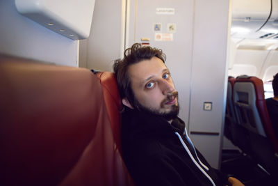Man in a black jacket with a hood is a passenger of the plane sitting on a chair