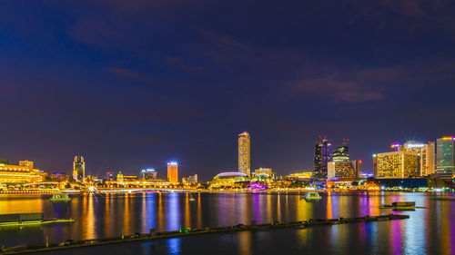 Illuminated buildings by river against sky at night