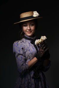 Portrait of woman wearing hat standing against black background