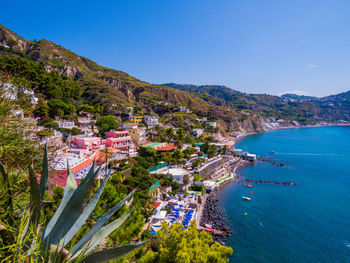 High angle view of buildings by sea against clear blue sky