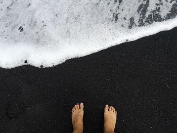 Low section of person standing on black sand beach