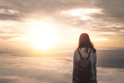 Rear view of woman standing against sky during sunset