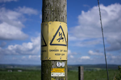 High voltage sign on wooden pole against sky