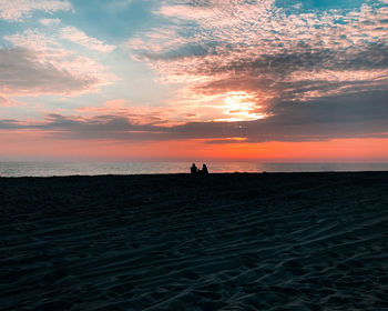 Silhouette people on beach against sky during sunset