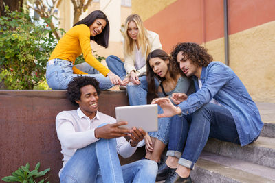 Friends using digital tablet while sitting on steps