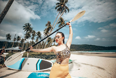 Young woman with arms raised at beach against sky
