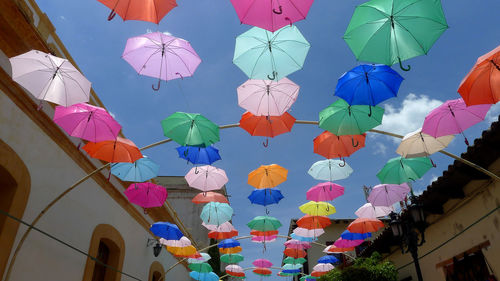 Low angle view of multi colored umbrellas hanging against building