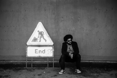 Bearded man sitting by sign against wall