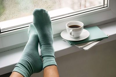 Coffee cup, books and woman legs against wet window. rest and reading at rainy day.