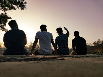 Rear view of people sitting on land against clear sky