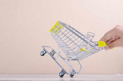 Cropped hand of person holding miniature shopping cart on table