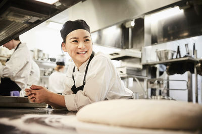 Smiling female chef leaning on counter in commercial kitchen