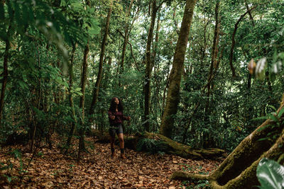 Ethnic female tourist looking up under high green trees in forest of monte verde in costa rica during trip