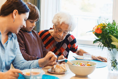 Great grandmother and mother looking at boy using smart phone in house