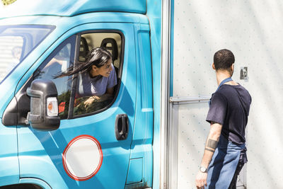 Male owner standing by colleague driving food truck in city