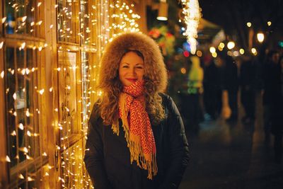 Portrait of woman standing by illuminated string lights on window at night