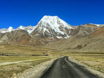 Road leading towards snowcapped mountain against clear blue sky