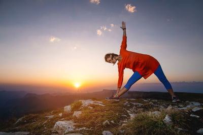 Woman in warrior pose in mountains, yoga practice outdoors at sunset