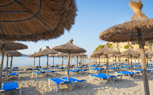 Lounge chairs and parasols on beach against clear sky