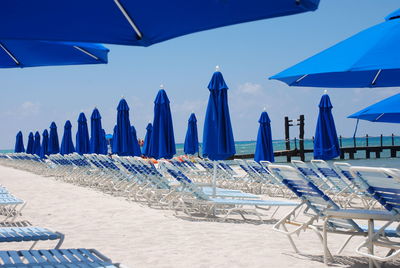 Row of chairs on beach against blue sky