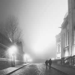 People walking on illuminated street against sky in city