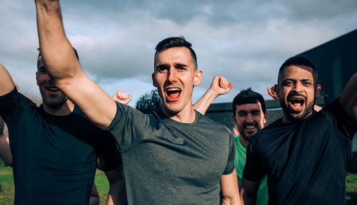 Men with arms raised screaming against sky