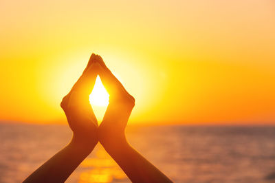 Cropped image of hand against orange sky during sunset