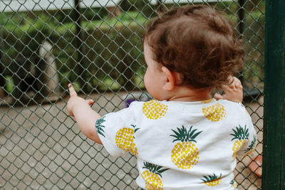 Rear view of boy looking through chainlink fence