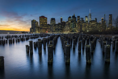Wooden posts in sea against sky at dusk. skyline in background. manhattan at dusk.