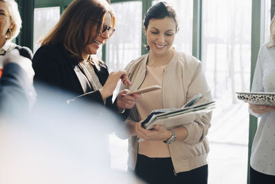 Smiling business people using smart phone while discussing in meeting at office