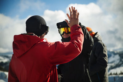 Friends in warm clothing high fiving against sky