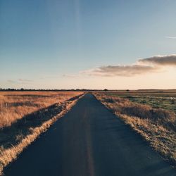 Single lane road on grassy field against sky