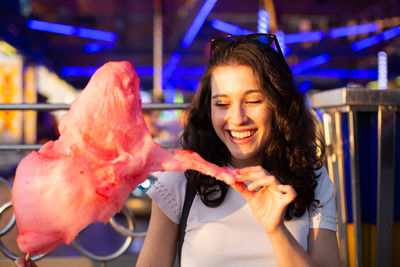 Smiling young woman holding ice cream at illuminated shop