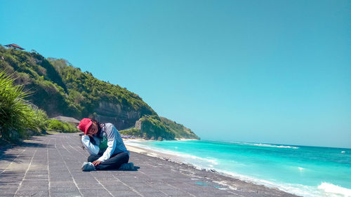 Full length of woman sitting on sea shore against clear sky