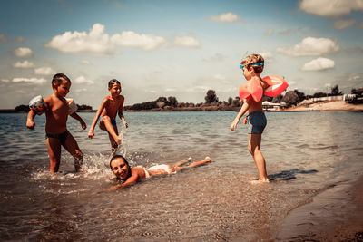 Playful kids and their mother having fun on the beach in summer.