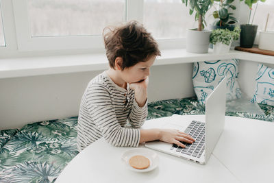 Little boy siting at the kitchen and look at the laptop. high quality photo