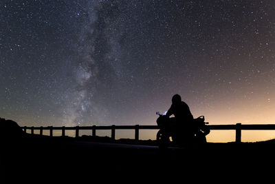 Silhouette man riding motor scooter against sky at night